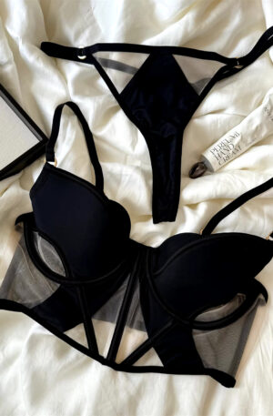 Black lingerie set with corset-style bra and thong, showcasing a mix of opaque and transparent fabrics, displayed on a mannequin.